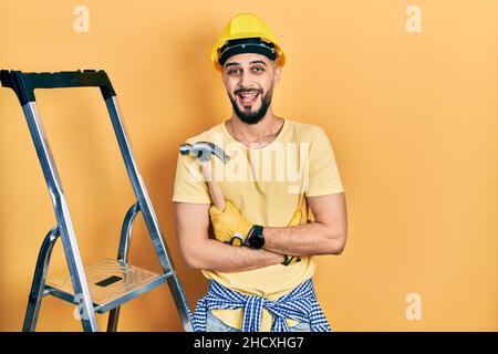 Handsome man with beard wearing hardhat holding hammer by stairs celebrating crazy and amazed for success with open eyes screaming excited. Stock Photo