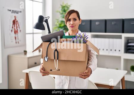 Middle age doctor woman holding cardboard box with items at the clinic skeptic and nervous, frowning upset because of problem. negative person. Stock Photo
