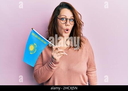 Young caucasian woman holding kazakhstan flag scared and amazed with open mouth for surprise, disbelief face Stock Photo