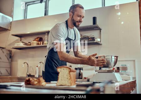 Cheerful man putting metal bowl on electronic scales Stock Photo