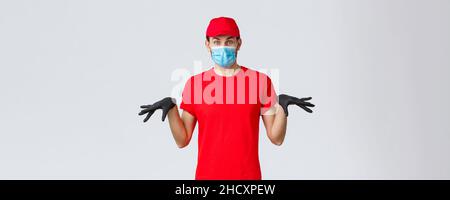 Covid-19, self-quarantine, online shopping and shipping concept. Funny courier in black rubber gloves and face mask, delivery guy in uniform gesturing Stock Photo