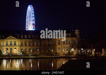 Stuttgart, Germany - December 31, 2021: Ferris wheel behind old castle at night. Lights reflecting in the pond water. Attraction in Stuttgart on the c Stock Photo