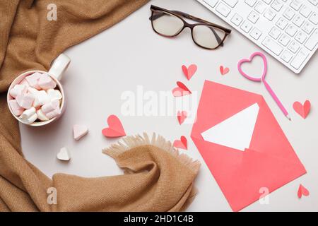 Top view of the desktop. Scarf glasses keyboard marshmallow envelope with valentine's day note on gray table. Flat lay copy space Stock Photo