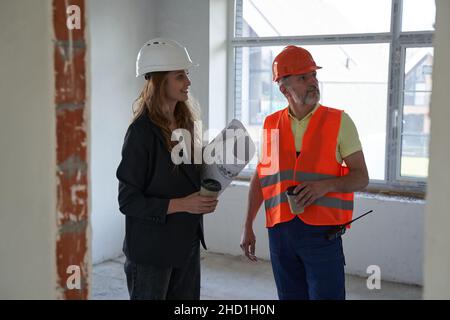Woman construction engineer and mature builder looking to side of room while keeping coffee cups in hands Stock Photo