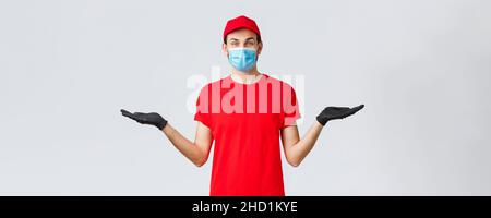 Groceries and packages delivery, covid-19, quarantine and shopping concept. Friendly delivery man in red uniform, face mask and gloves, holding two Stock Photo