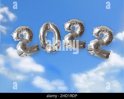 Year 2022 written with silver metallic balloon numbers floating in the air with blue sky and white light clouds. Concept of prospects for the year wit Stock Photo