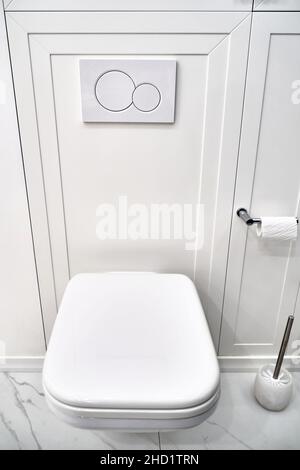 Elegant contemporary toilet bowl with tank hidden behind white panel and flush buttons on wall in light restroom close view Stock Photo
