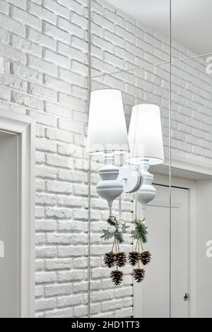 Vintage chandelier with Christmas ornate and glowing lamp on mirror wall near white brick wall with door in light room of luxury apartment closeup Stock Photo
