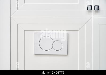 Stylish flush buttons of contemporary toilet bowl tank hidden behind white panel on wall in light restroom extreme close view Stock Photo