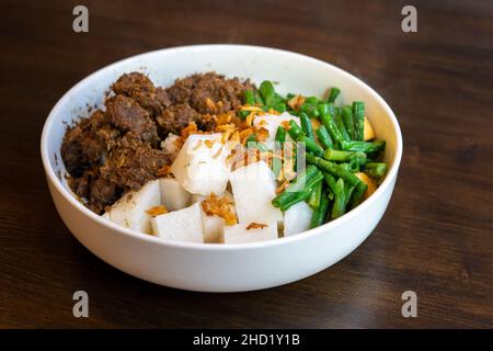 A plate of Javanese food with beef rendang , lontong rice and green beans on white plate Stock Photo