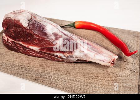 Fresh raw lamb shank. Fresh raw lamb bone on wooden cutting board and stick of red hot raw pepper Stock Photo