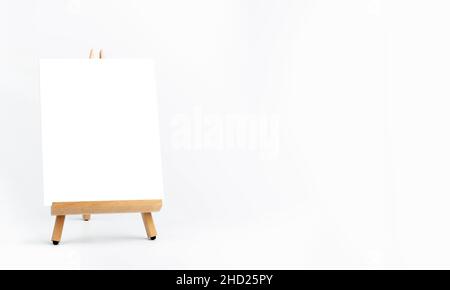 White blank artist frame on a small wooden easel on white background with copy space. Advertising mockup artboard for pictures or artwork. Painting fr Stock Photo