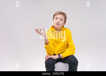 Handsome smiling young european guy teenager speechlessly looking at camera shocked by high prices, wearing casual bright yellow hoodie isolated on white background Stock Photo