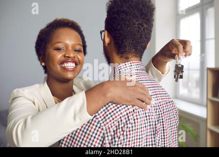 Happy young black woman hugging her husband, holding key to new house and smiling Stock Photo