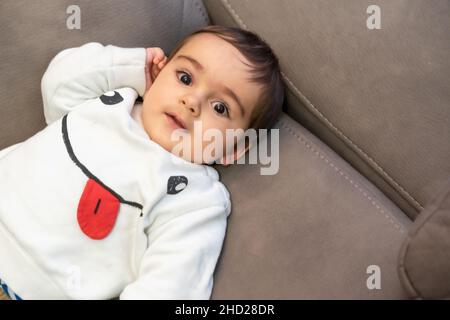 Baby crying with the pain of his first teeth, lying on the sofa at home Stock Photo