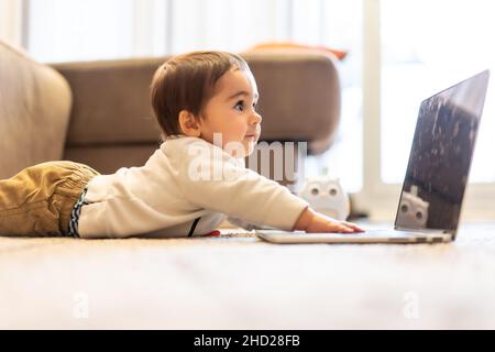 Baby lying on the floor having fun playing on his father's work computer Stock Photo