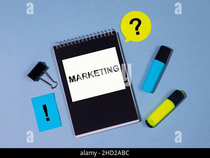 text Marketing on black notepad with clips, markers, sticker on blue table. Business concept Stock Photo
