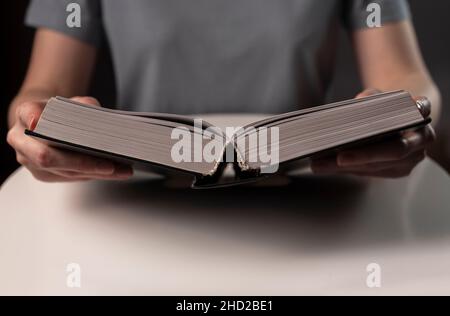 Female hands close up, holding and reading book or textbook in hard cover. Stock Photo