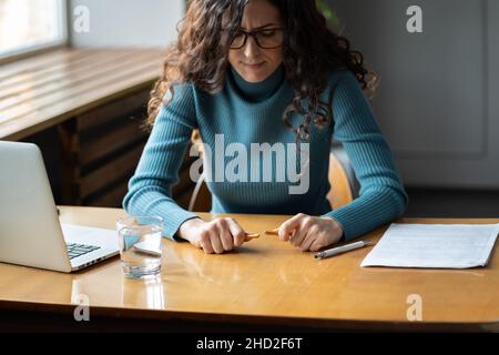 Young stressed woman at workplace with broken pencil, worried female employee feeling nervous Stock Photo