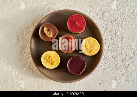 Blueberry, raspberry, lemon, goji and banana raw vegan mini cheesecakes on a plate on white background Stock Photo