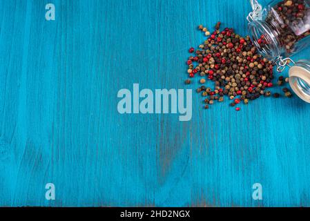 Blue wooden background with a lying pot with multi-colored peppercorns.Copy space. Stock Photo