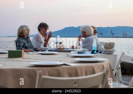 Malaga, Andalucia, Spain. June, 2021.  Group of tourists sitting in a restaurant in front of the port of Malaga at sunset. Stock Photo