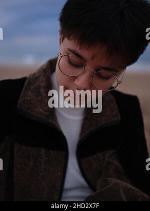 transgender woman with glasses and nose piercing resting looking at the ground Stock Photo