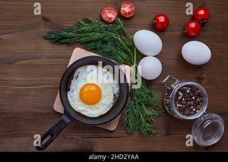 Fried egg in a small skillet with a stand, a bunch of dill, tomatoes Stock Photo