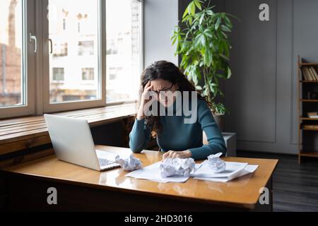 Overwhelmed tired businesswoman sit at desk with laptop and crumpled paper frustrated and exhausted Stock Photo