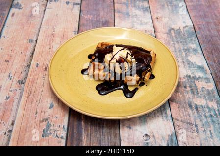 Crispy wafer-shaped biscuit of Belgian origin that is cooked between two dishes, to this a scoop of vanilla ice cream and a lot of chocolate syrup wer Stock Photo