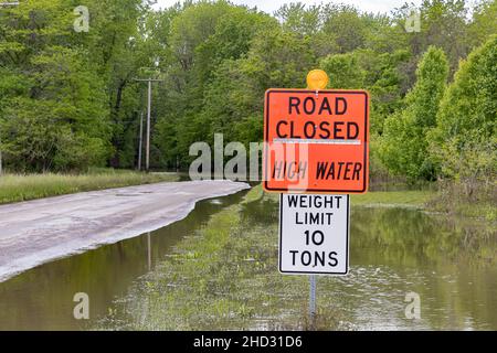 Road closed sign and high water flooding roadway. Storm and rain damage, weather warning and climate change concept. Stock Photo