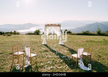 Wedding arch decorated with flowers and curtains stands on the mountain in front of the chairs Stock Photo