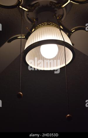 Low angle closeup shot of a ceiling fan with the light turned on and wires hanging in a hotel room Stock Photo