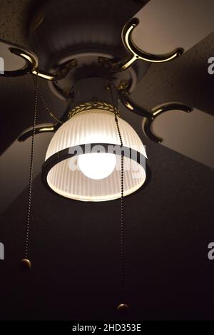 Low angle closeup shot of a ceiling fan with the light turned on and wires hanging in a hotel room Stock Photo