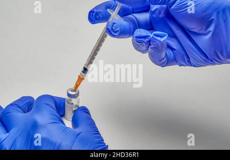 Hands with blue gloves, holding a vial to which they are introducing a liquid with a syringe. Stock Photo