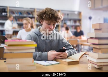 Teenage boy with smartphone in library Stock Photo