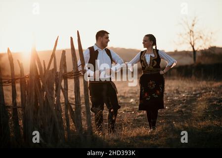 Young multi-racial couple dancing in a Serbian traditional costume in a field in Serbia Stock Photo