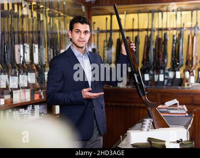 Handsome adult male in hunting shop with rifle in hands Stock Photo