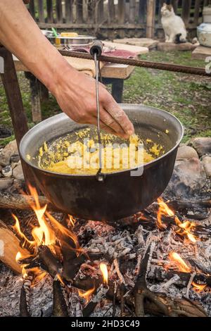 Polenta or mamaliga cooking on an open fire in a large pot. Stock Photo