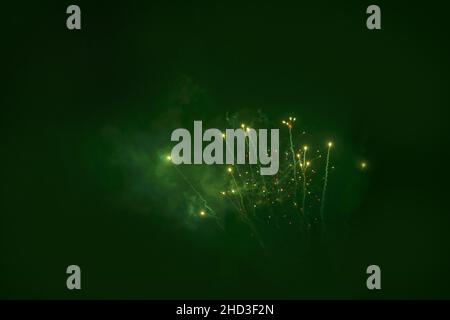 green fireworks in the sky at night with lights and smokes Stock Photo