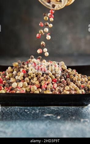 Multi-colored peppercorns are poured on top into plate of pepper Stock Photo