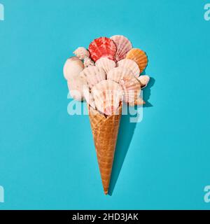 Summer holiday design with colorful seashells and ice cream cone on blue background. Creative minimal beach food concept with flat lay view. Stock Photo
