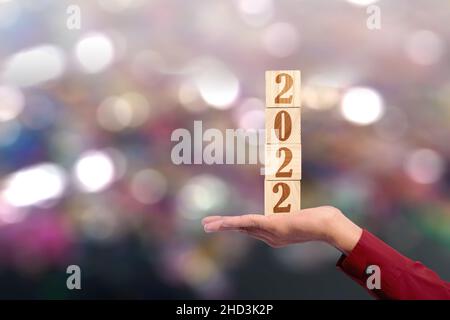 Hand showing 2022 on a wooden cube with blurred light background. Happy New Year 2022 Stock Photo