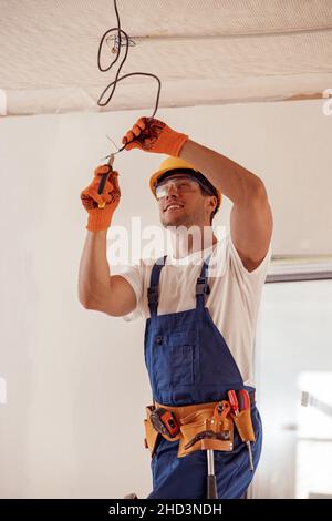 Cheerful electrician repairing electric cable on ceiling Stock Photo