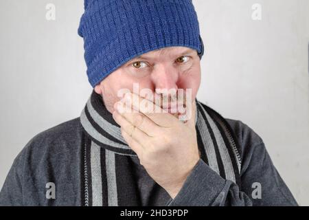 A man is experiencing a toothache. An adult male is holding his lower jaw with his hand. Health and Medicine.  Indoors. Stock Photo