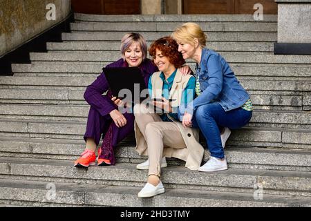 Live streaming classes using laptop by three middle aged women outdoors. Stock Photo