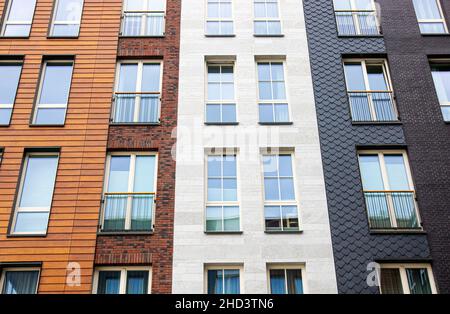 Modern apartment building exterior facade with lot of different materials: wood, stone bricks. Lot of white frame windows. Stock Photo
