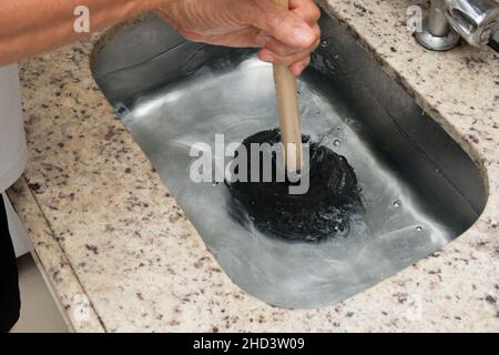 Closeup of the man using a plunger to unstop the kitchen sink. Stock Photo