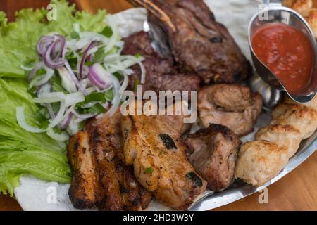 Assorted delicious grilled meat with lettuce and onion. Mixed grilled bbq meat with tomato sauce.Lamb, chicken. Top view, close up with copy space. Stock Photo