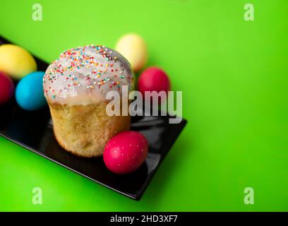Easter themes. Multi-colored eggs on a bright and baked kulich grassy green background. Copy space for text. Stock Photo